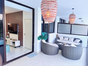 A modern living room with a sofa, two round wicker chairs, a large potted plant, and a flat-screen TV mounted on the wall. - Cana Bay | Near Hard Rock & Beach Club (Punta Cana)