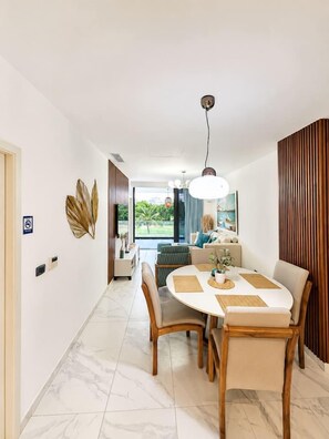 Ein modernes Interieur mit einem Essbereich, der einen runden Tisch und Stühle umfasst, einem Flur, der zu einem Wohnbereich mit Aussicht führt, und einer Wand mit Holzverkleidung.