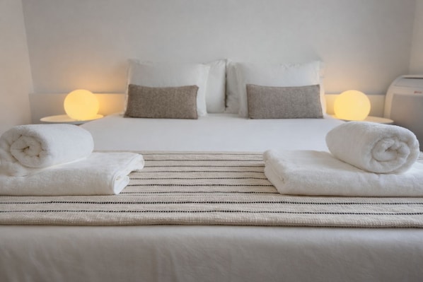 Ein Hotelzimmer mit einem Bett, zwei Kissen, zwei zusammengerollten Handtüchern, einem Nachttisch und einer Lampe.