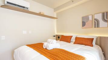 Habitación de hotel con cama, aire acondicionado de pared, estante y arte abstracto en la pared.