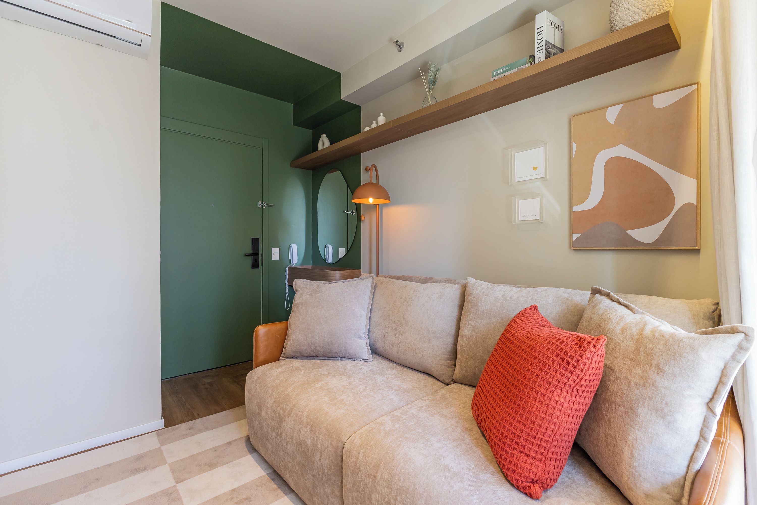 Una sala de estar con un sofá color crema, un cojín rojo, una estantería de madera con adornos y un cuadro en la pared.