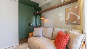Una sala de estar con un sofá color crema, un cojín rojo, una estantería de madera con adornos y un cuadro en la pared.