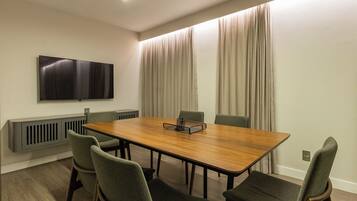 Un salón de conferencias con una larga mesa, cuatro sillas, un televisor de pantalla plana y una ventana con cortinas.