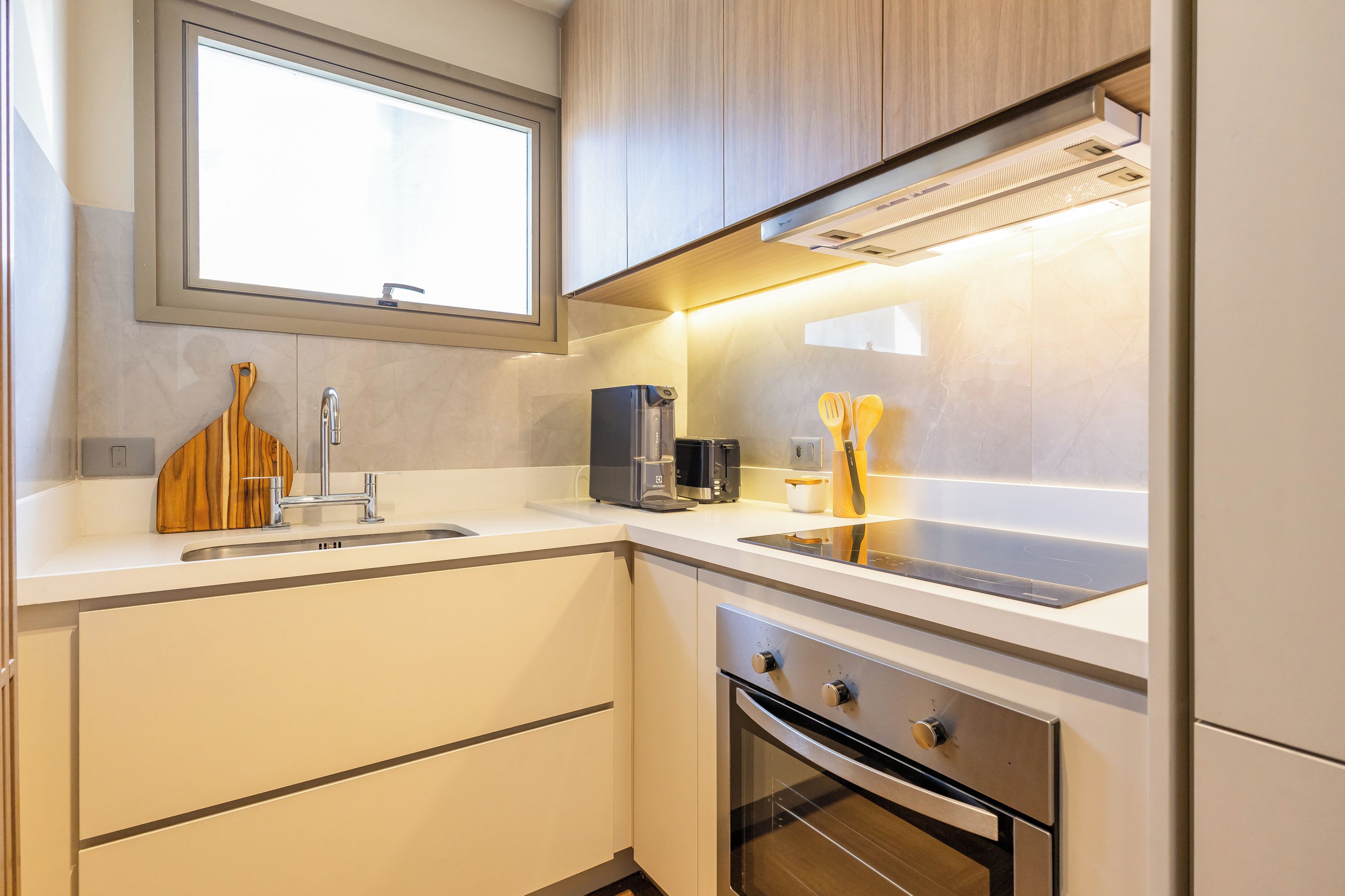 Una cocina moderna con horno empotrado, cafetera y utensilios de madera sobre la encimera.