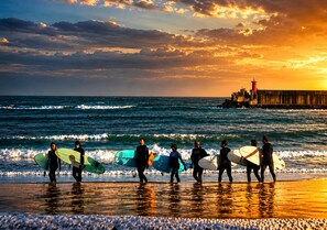 Eine Strandansicht mit Surfern, die mit Surfbrettern auf das Meer zugehen.