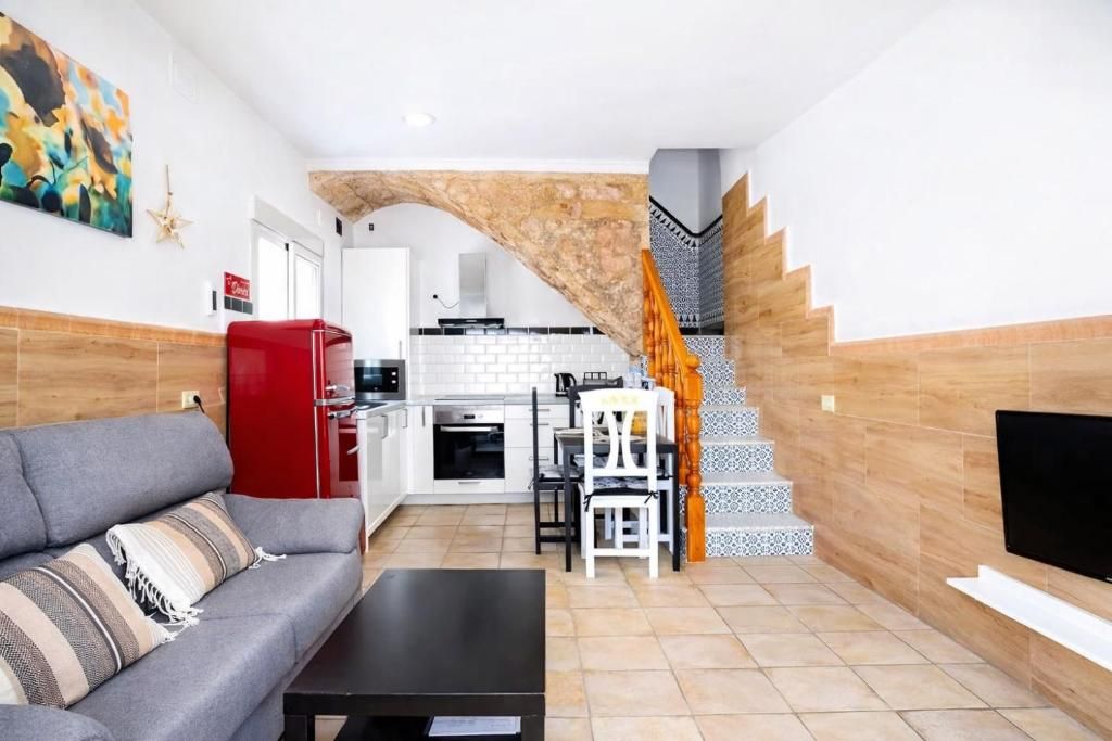 A living room with a sofa, a coffee table, a kitchen in the background, and a staircase with patterned tiles.