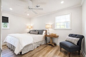 Een slaapkamer met een bed, nachtlampjes, een stoel en een plafondventilator.