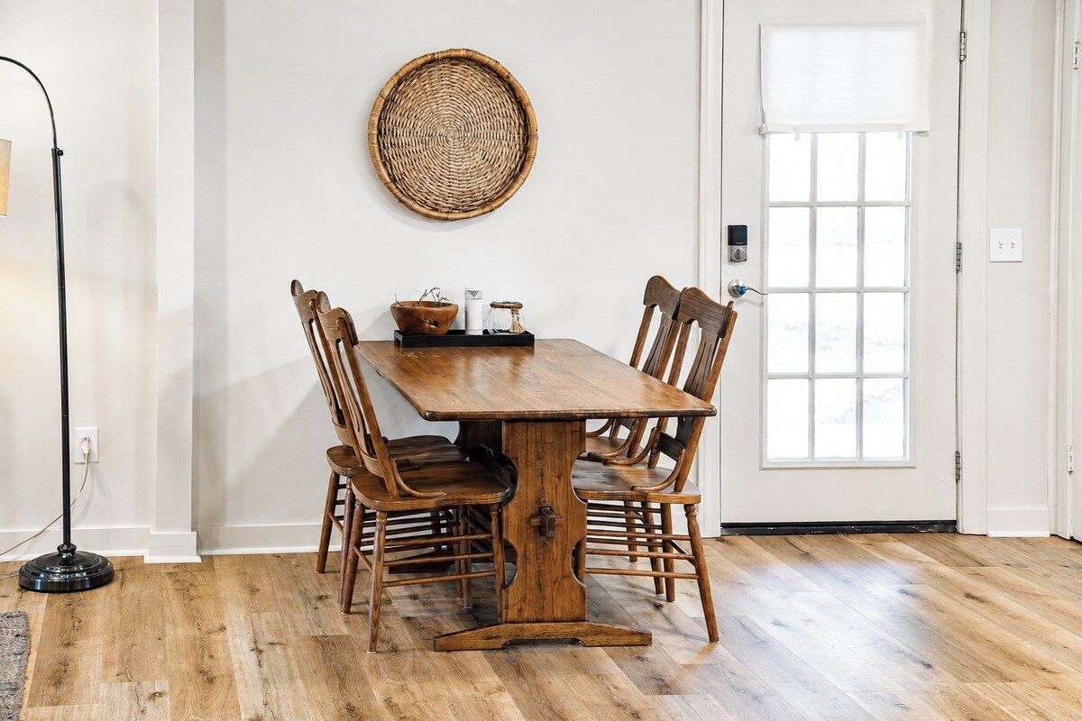A dining area with a wooden table and chairs, a woven wall hanging, and a window with a view.
