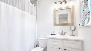 Et badeværelse med toilet, vask med spejl og bruseforhæng.