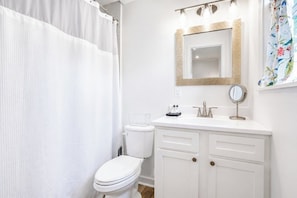 A bathroom with a white toilet, a white sink with a mirror, and a shower curtain. - The Birdhouse, Pet-Friendly 3BR by Velvet Ditch (Oxford)