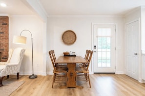 A dining area with a wooden table and chairs, a floor lamp, a woven wall hanging, and a door with a window. - The Birdhouse, Pet-Friendly 3BR by Velvet Ditch (Oxford)