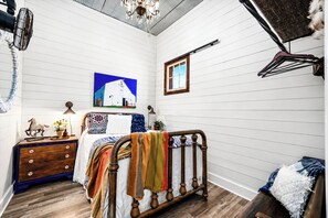 A bedroom with a wooden bed, a dresser, a painting of a barn, and a window.
