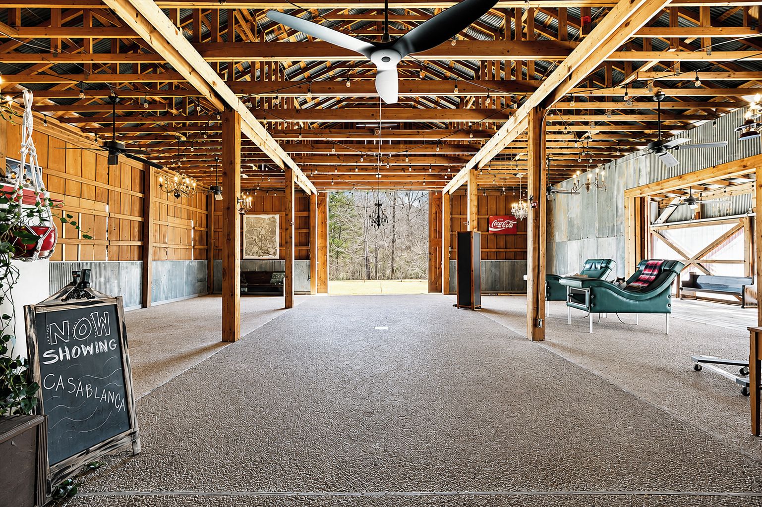 An interior with exposed wooden beams, a ceiling fan, and a seating area with lounge chairs.
