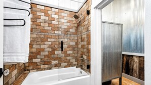 Un bagno moderno con parete doccia in mattoni, una vasca da bagno bianca e una porta in metallo.