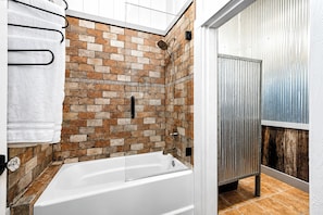 A modern bathroom with a brick-patterned shower wall, a white bathtub, and a metal door. - The Barn, Pool + Private Theater by Velvet Ditch Villas (Oxford)