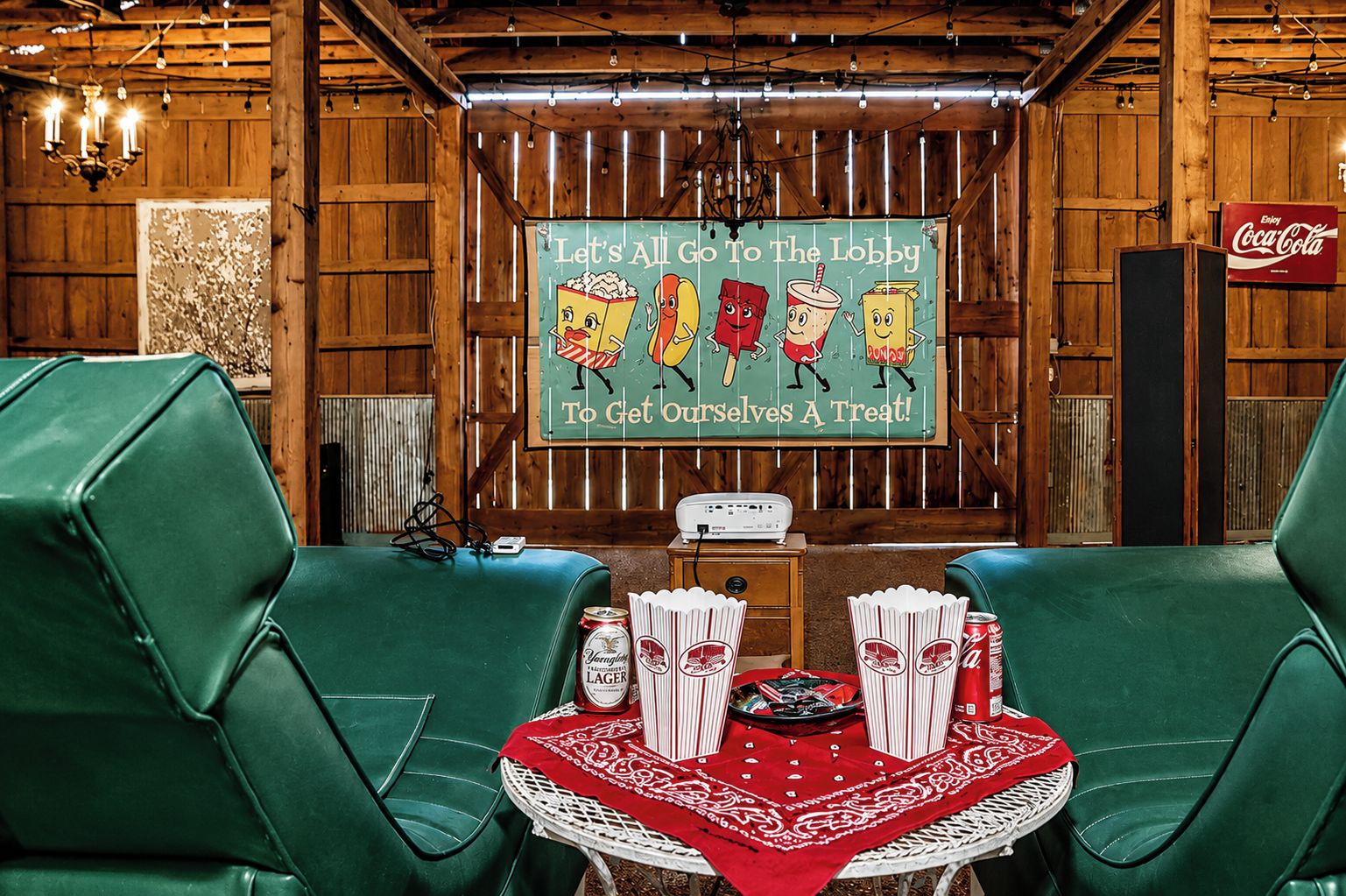 A lobby with wooden paneling, a Coca-Cola sign, green leather chairs, a table with snacks, and a sign inviting guests to the lobby.