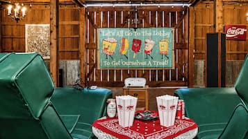 A lobby with wooden paneling, a Coca-Cola sign, green leather chairs, a table with snacks, and a sign inviting guests to the lobby.