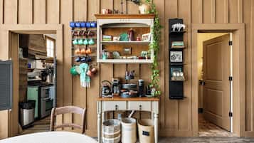 A kitchen with wooden paneling, a hanging pot rack, a coffee station, and a door leading to another room.