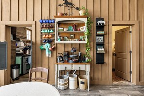 A kitchen with wooden paneling, a hanging pot rack, a coffee station, and a door leading to another room.