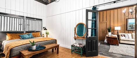A bedroom with a bed, bedside table, lamp, and a view into another room.