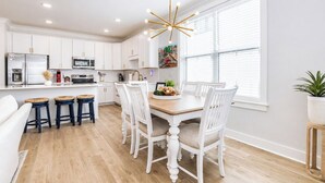 A modern kitchen with white cabinetry, a central island, and a dining area with a wooden table and white chairs. - The Rebel Hideout, Pool+3BR | Velvet Ditch Villas (Oxford)