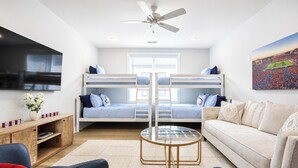 A room with bunk beds, a flat-screen TV, a ceiling fan, a glass coffee table, and a sofa. - The Rebel Hideout, Pool+3BR | Velvet Ditch Villas (Oxford)
