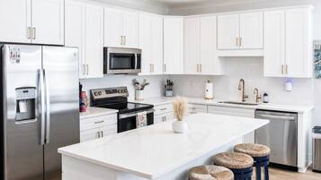 Una cucina moderna con mobili bianchi, elettrodomestici in acciaio inossidabile, un'isola centrale con sgabelli e un forno a microonde integrato.