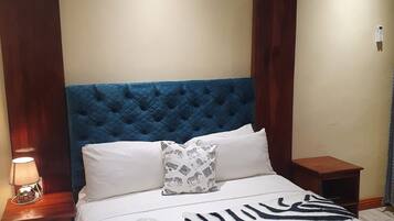 A hotel room with a tufted headboard, a zebra-patterned throw, a white pillow with a zebra print, and a bedside lamp.