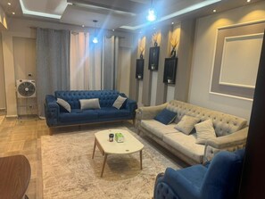 A living room with two sofas, a coffee table, and a fan. - Modern 2BR in 6th October Balcony, Parking, WiFi & Smart TV (6th October)