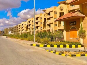 A residential building with multiple balconies, a gated entrance, and a clear sky. - Modern 2BR in 6th October Balcony, Parking, WiFi & Smart TV (6th October)