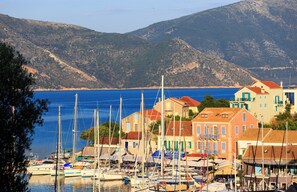 Une ville côtière aux bâtiments aux couleurs vives, un port de plaisance rempli de bateaux et un paysage montagneux en toile de fond.