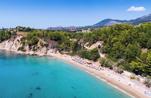 A coastal beach with clear turquoise waters, a sandy shore, and a row of beach umbrellas. - Stylish New Villa with Sea Views Walk to Beach (Livathou)