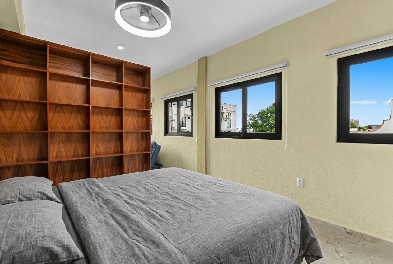 Een slaapkamer met een bed, een houten inbouwplank en twee ramen.