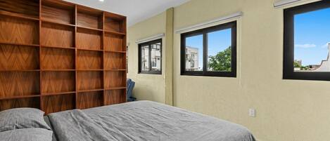 Un dormitorio con cama, estantería empotrada de madera y dos ventanas.
