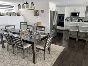 Una cucina moderna con mobili bianchi, elettrodomestici in acciaio inossidabile e un'area pranzo con un tavolo e sedie in legno scuro.