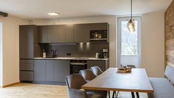 A modern kitchen with dark cabinetry, a wooden dining table, and a built-in oven.