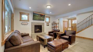 A spacious living room with leather sofas, a fireplace, a television, and a staircase.