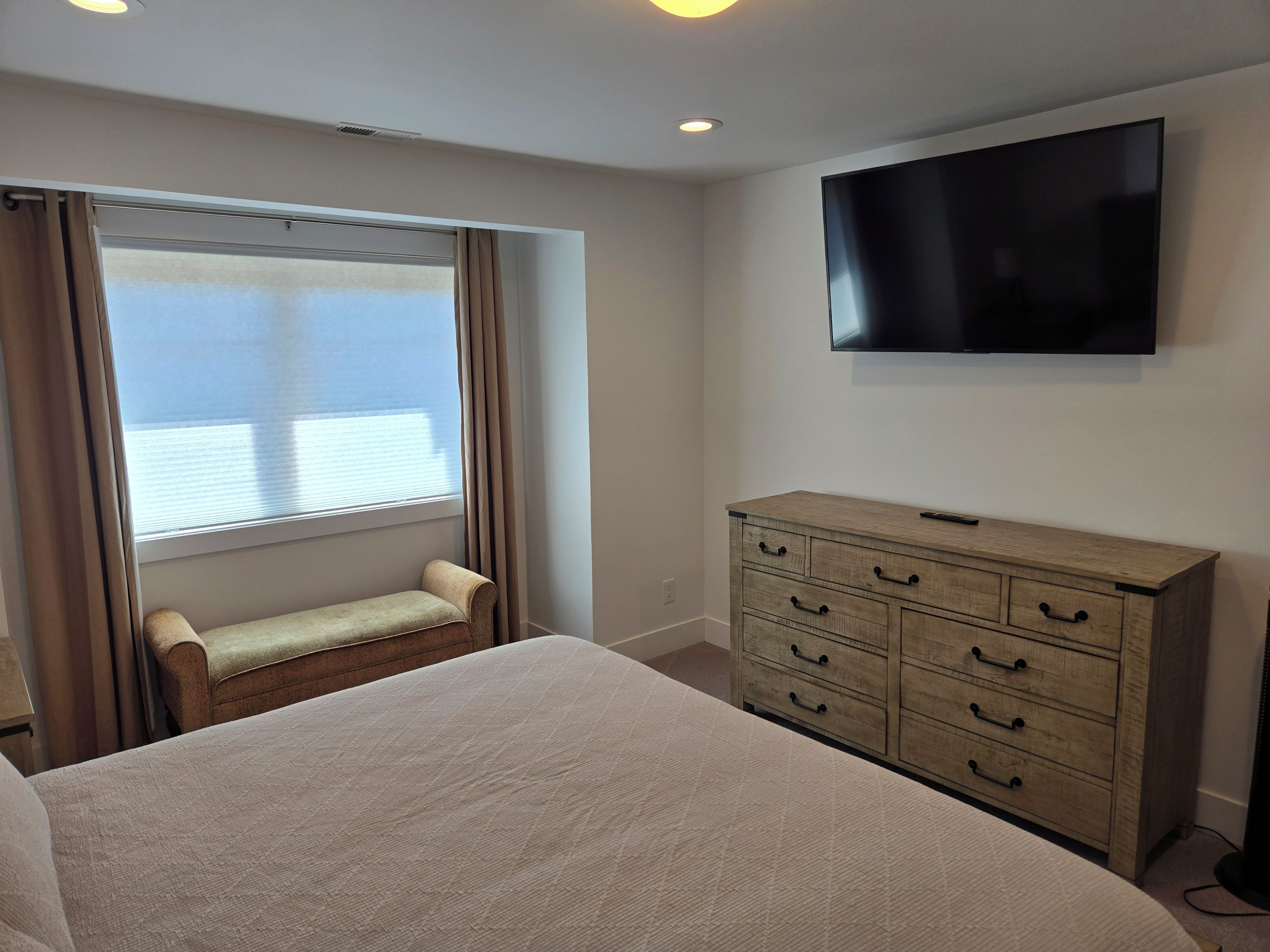 A hotel room with a bed, a wooden dresser, a television, and a window with curtains.