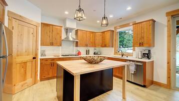 A modern kitchen with wooden cabinets, a central island, stainless steel appliances, and pendant lighting.