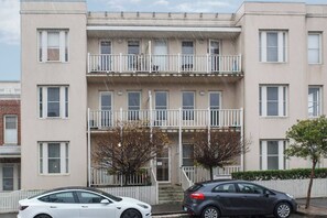 Ein mehrstöckiges Wohnhaus mit Balkonen, einem weißen Zaun und zwei geparkten Autos davor.