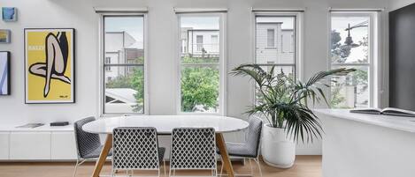 A modern dining area with a round table and chairs, large windows, and a potted plant.