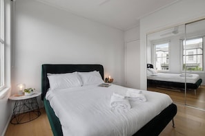 Ein modernes Hotelzimmer mit einem großen Bett, einem Nachttisch mit Lampe und einem Spiegel, der den Raum widerspiegelt.