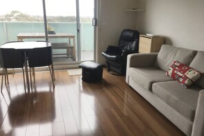 A living room with a sofa, a black leather chair, a small table, and a sliding glass door leading to an outdoor area. - Highview on High St A Balcony Haven in Northcote (Northcote)