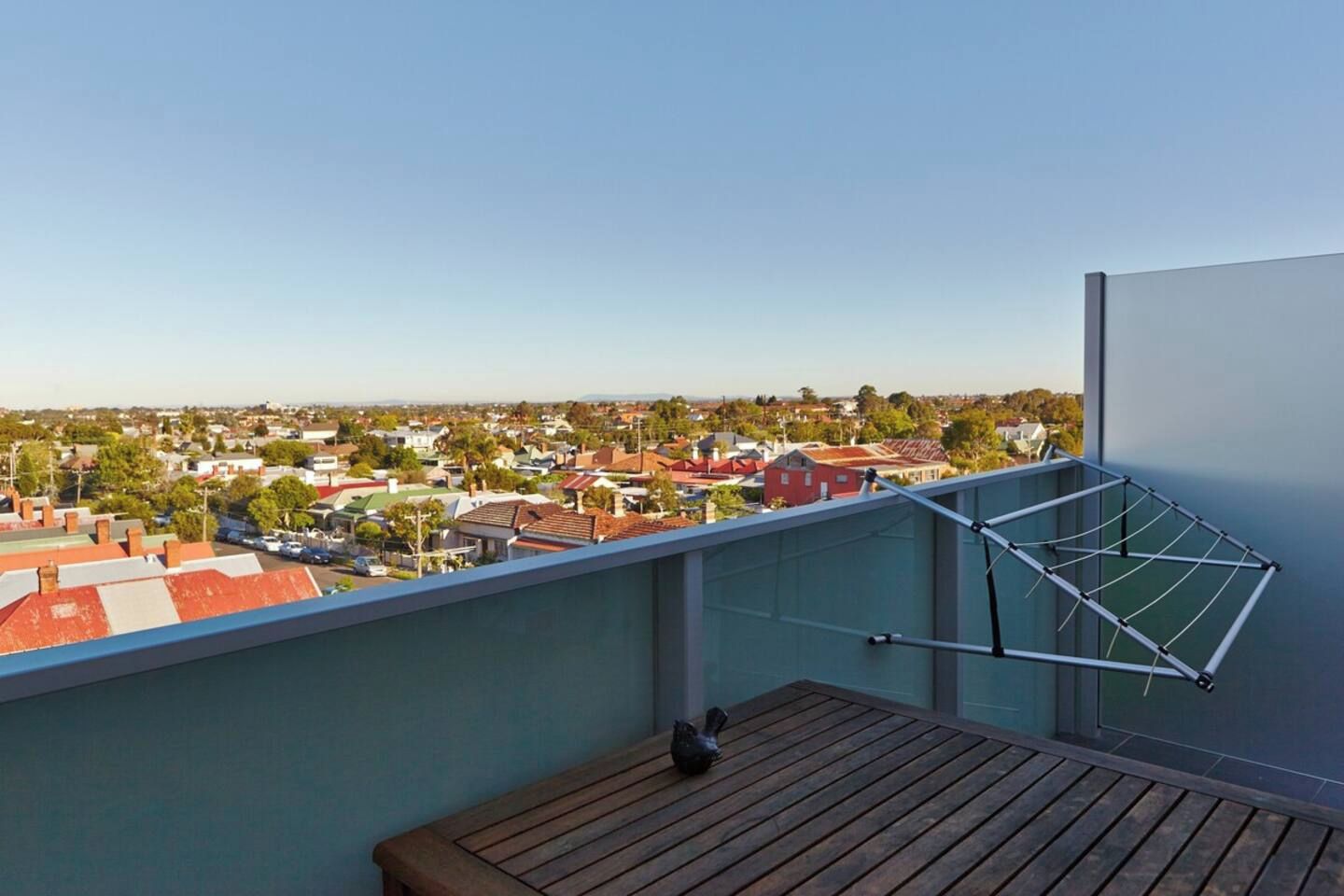 A balcony with a view of a residential area, a drying rack, and a wooden table.