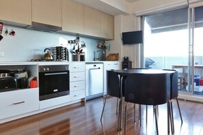 A modern kitchen with white cabinets, a black stove, and a dining area with a black table and chairs. - Highview on High St A Balcony Haven in Northcote (Northcote)