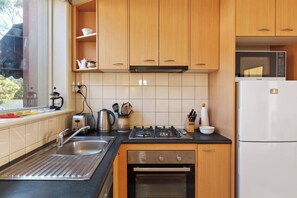 Una cocina moderna con armarios de madera, estufa a gas, horno empotrado, un lavamanos y un microondas.
