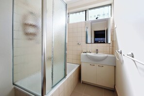 Un bagno con box doccia in vetro, vasca, lavabo con articoli da toilette e specchio sopra il lavabo.