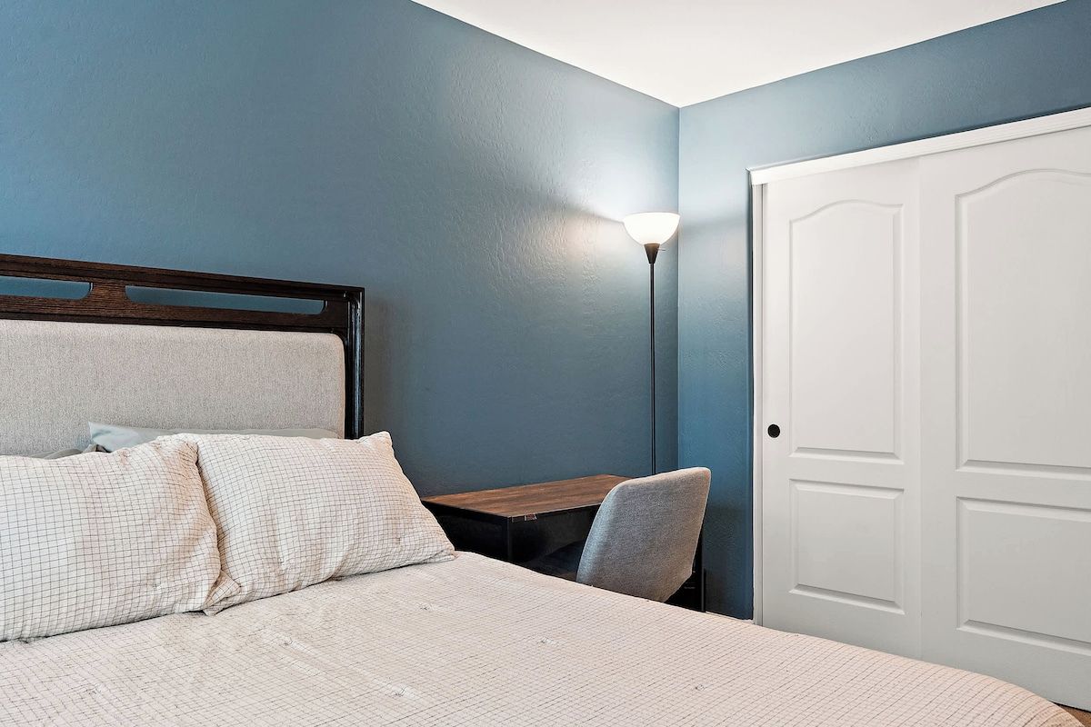 A bedroom with a bed, a desk, a chair, and a door.