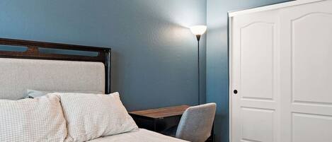 A bedroom with a bed, a desk, a chair, and a door.