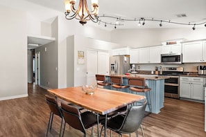 A modern kitchen with white cabinets, a central island, and a dining area with a wooden table and chairs. - Surprise House 🌵⛳ Fenced Pool & Firepit Near Surprise Stadium (Surprise)